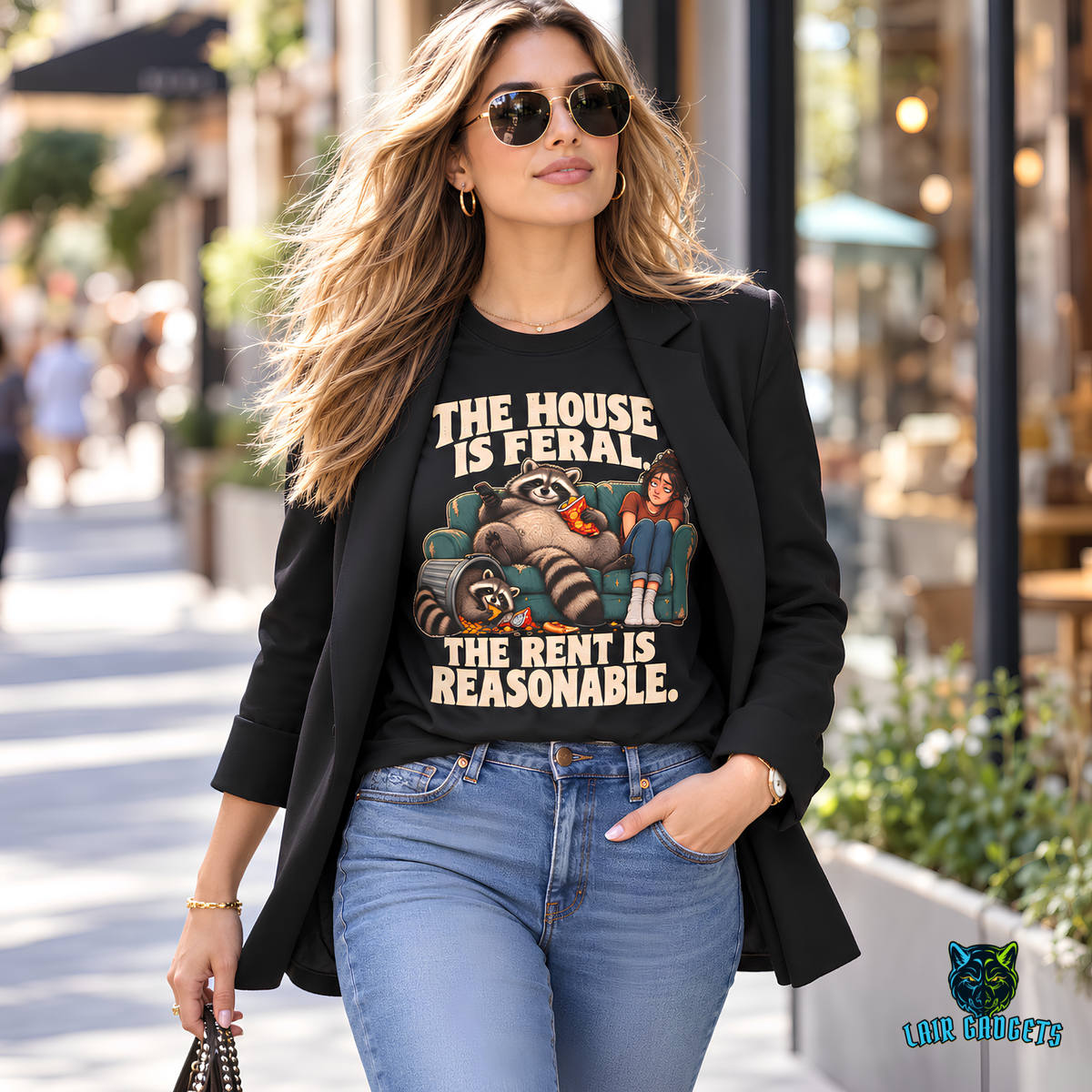 Model in a black tee reading The House Is Feral. The Rent Is Reasonable. with raccoons on a couch beside a woman