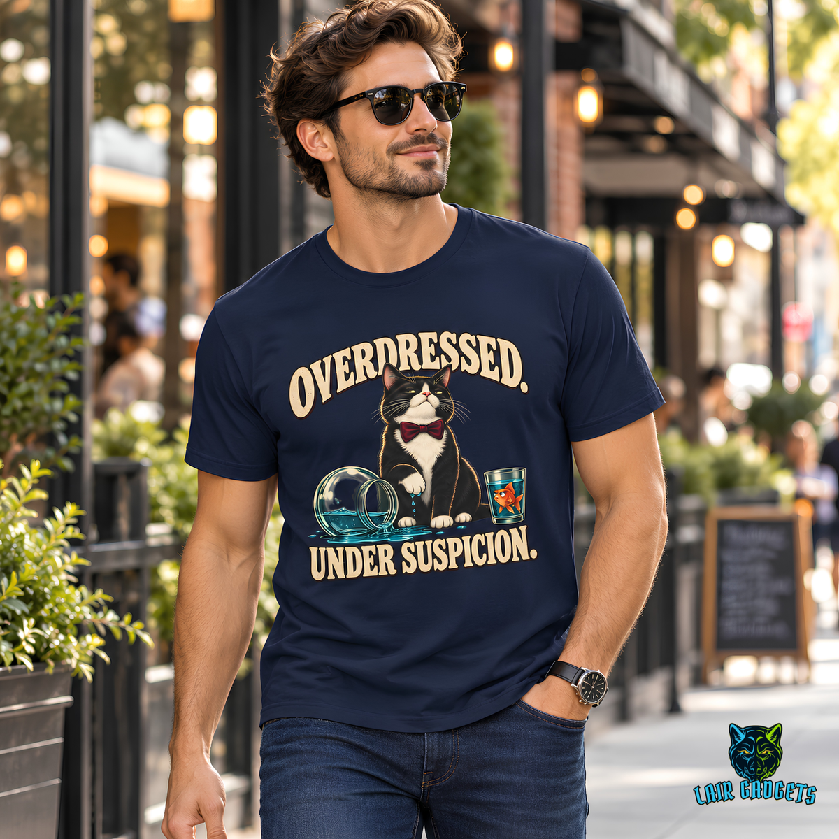 Model wearing an Overdressed. Under Suspicion. tee with a tuxedo cat in a bow tie beside a tipped fishbowl